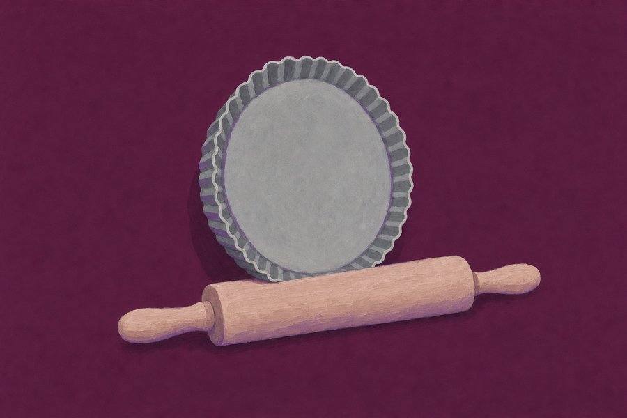 A round loose-bottomed fluted tart tin standing on edge behind a plain wooden rolling pin lying flat in front of it.
